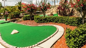 A miniature golf course with a green putting area, surrounded by landscaped gardens, palm trees, and a rocky backdrop. - Perfect Lakefront Serenity: Private Sunrise Views, just 1 mi. to Disney Springs! (Orlando)