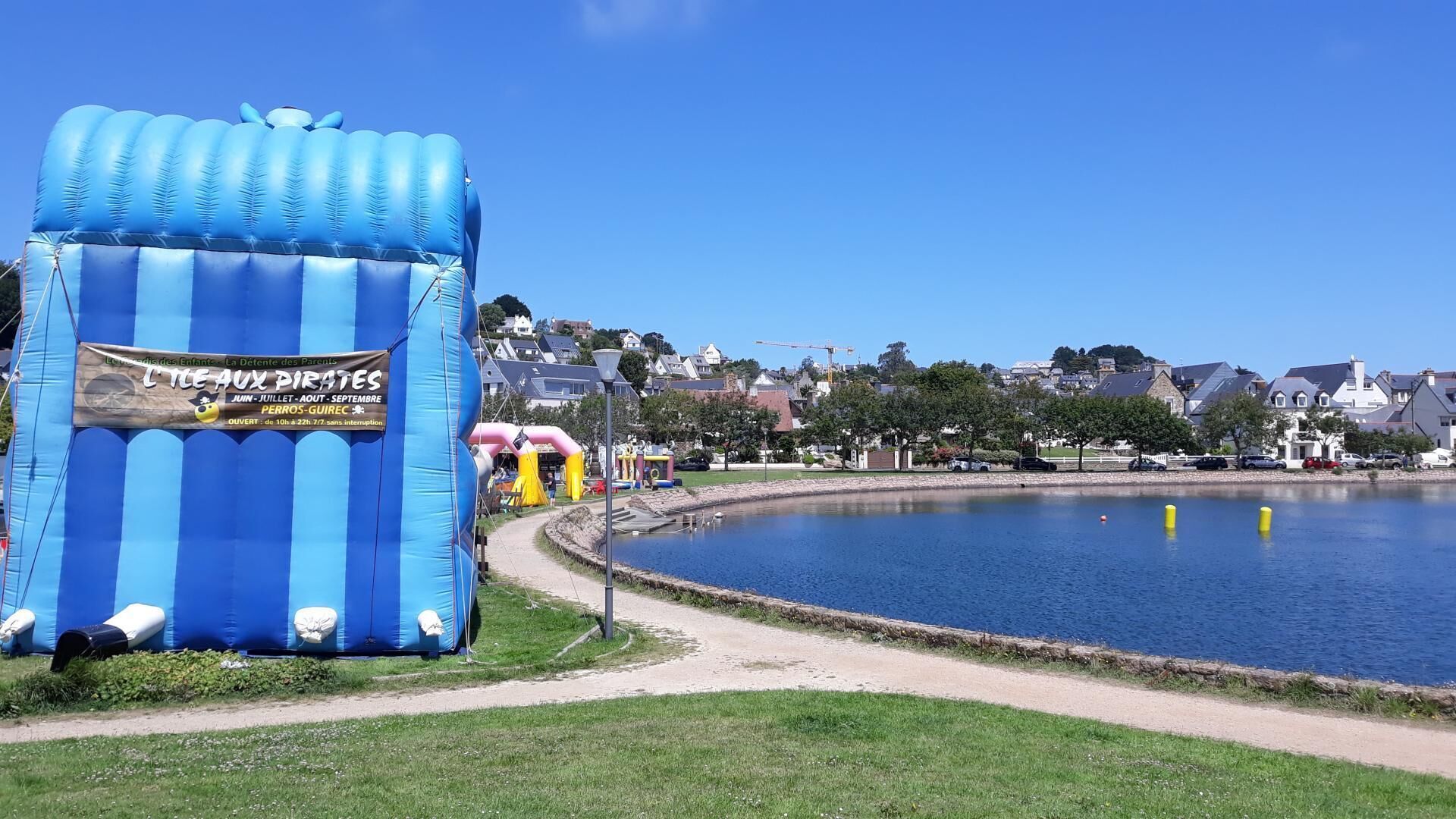 A blue inflatable structure with a sign, a pathway leading to a body of water, and houses in the background.