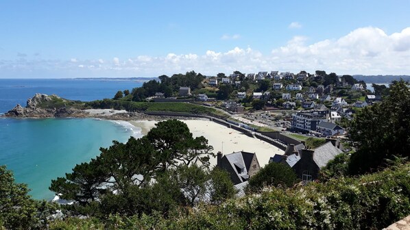 A coastal town with a sandy beach, houses, and a rocky outcrop.
