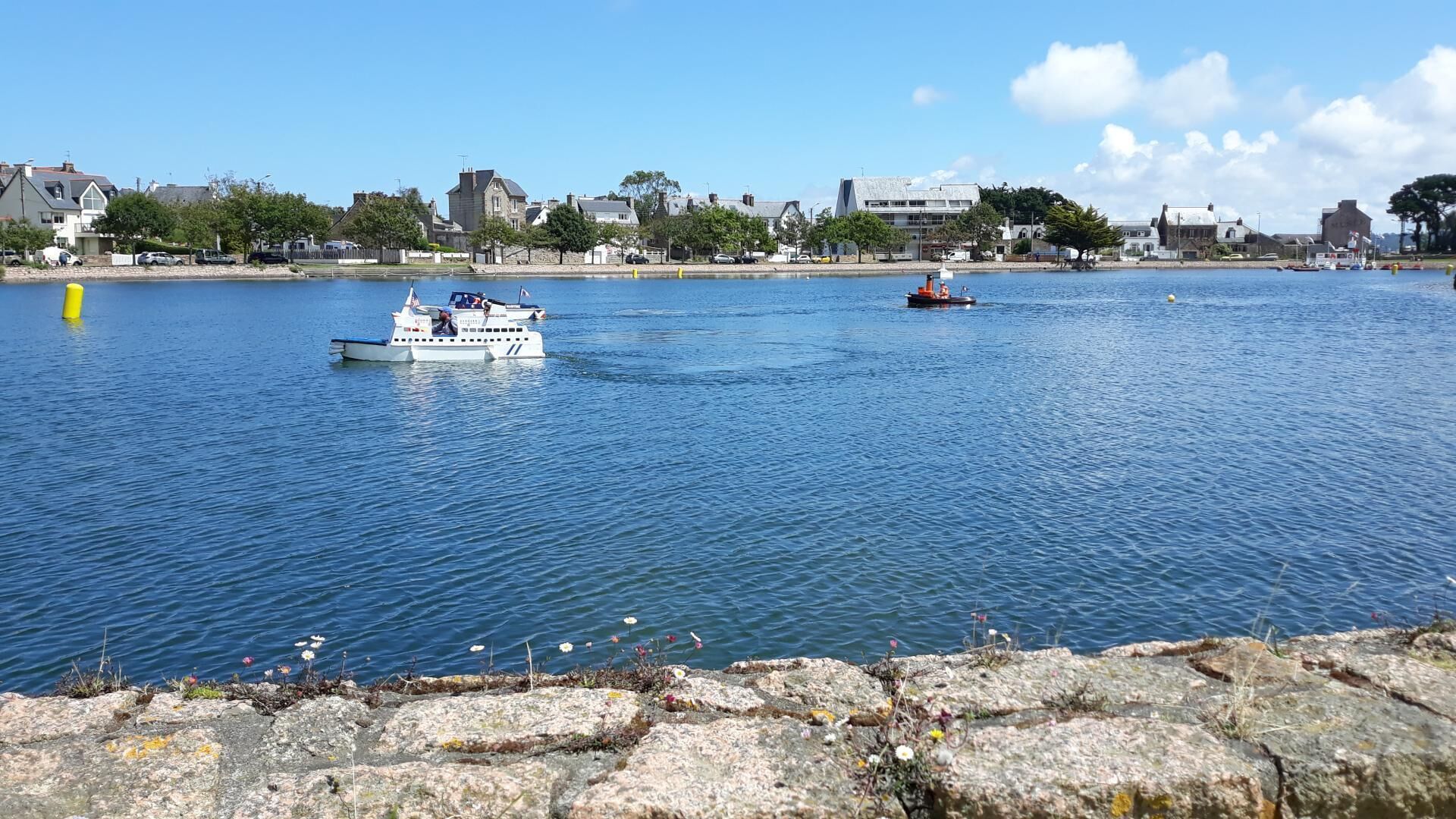 Un río tranquilo con barcos, una orilla rocosa en primer plano y edificios al fondo.