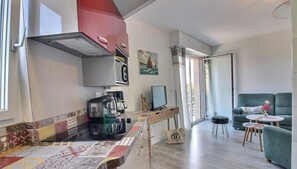 En kompakt opholdsstue med tekøkken, spiseplads og siddeområde med sofa og lille bord.