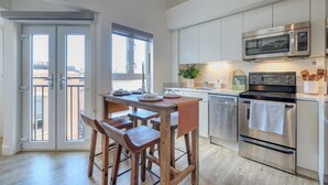 Una cocina moderna con una mesa de madera y taburetes de bar, electrodomésticos de acero inoxidable y vistas a través de grandes puertas correderas.