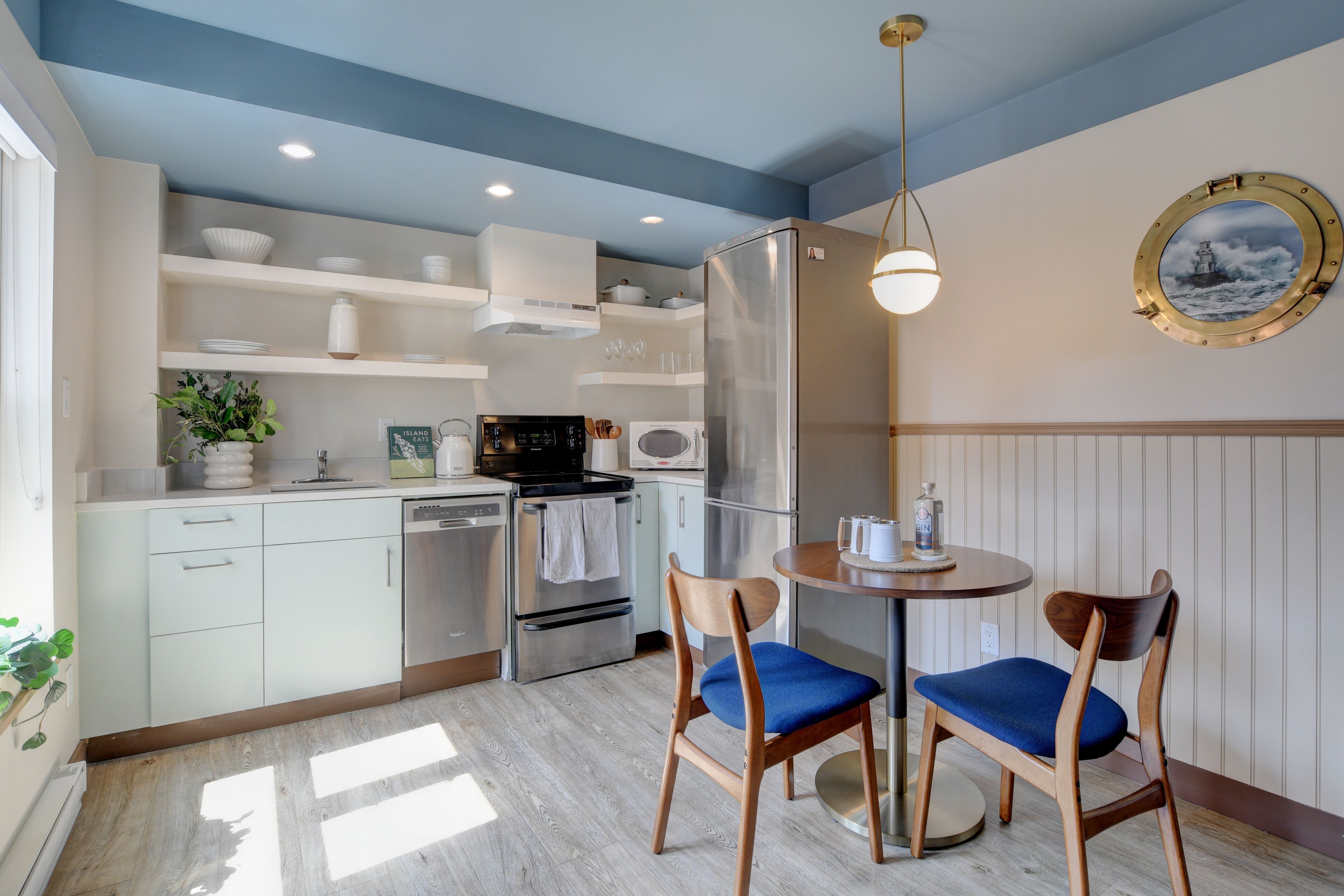 Une cuisine moderne avec des meubles blancs, des appareils en acier inoxydable et une table ronde entourée de chaises bleues.