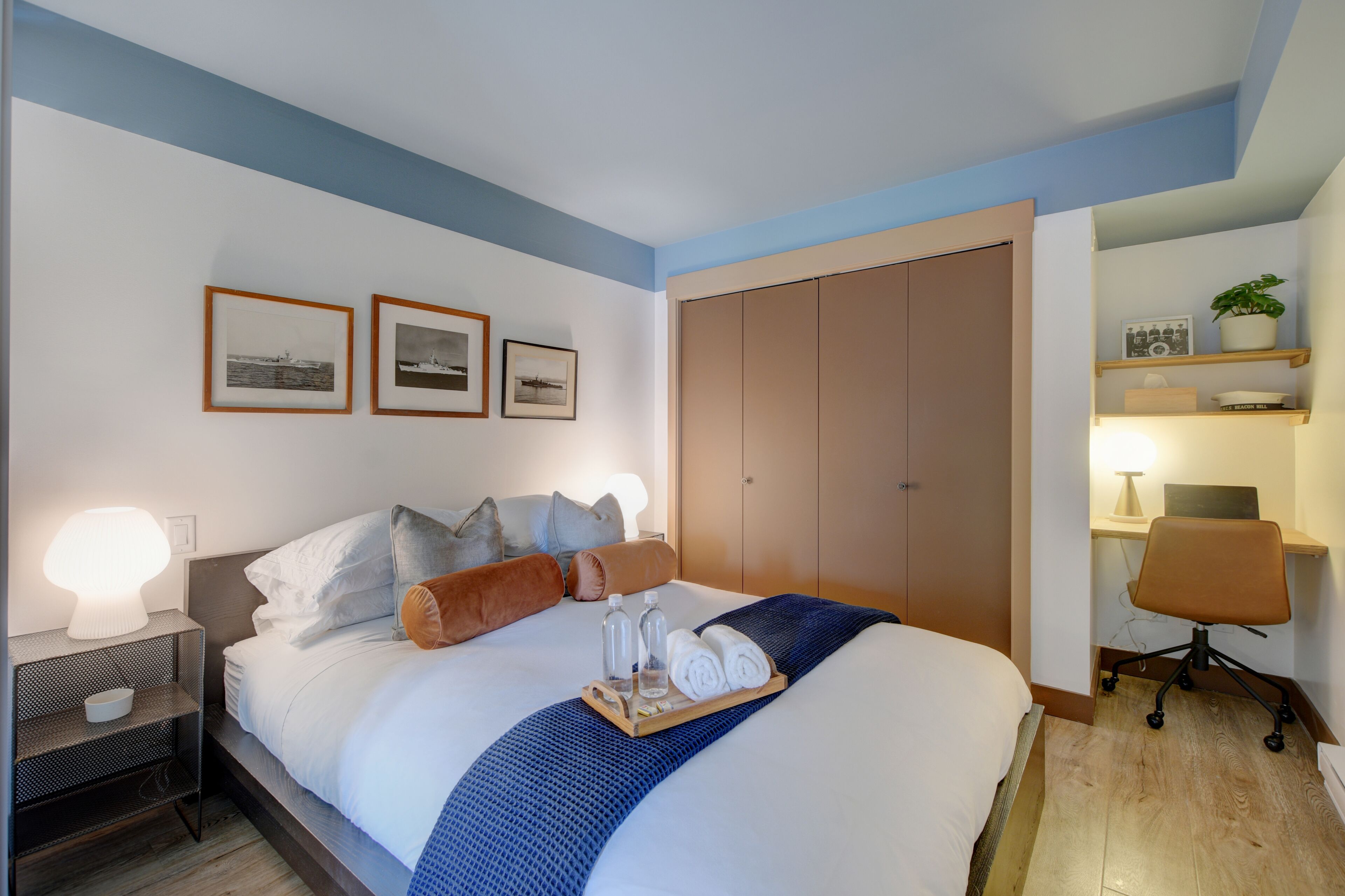 A hotel room with a bed, bedside tables, a desk, a chair, and a wardrobe.