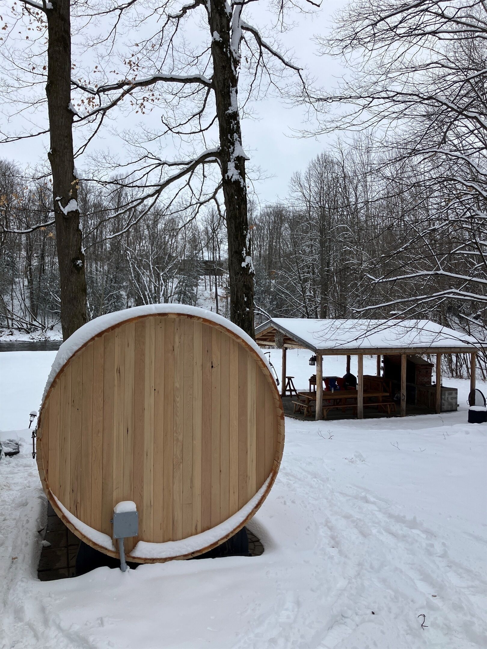 Een houten sauna met een bank en een overdekte zithoek, gelegen in een besneeuwd bos.