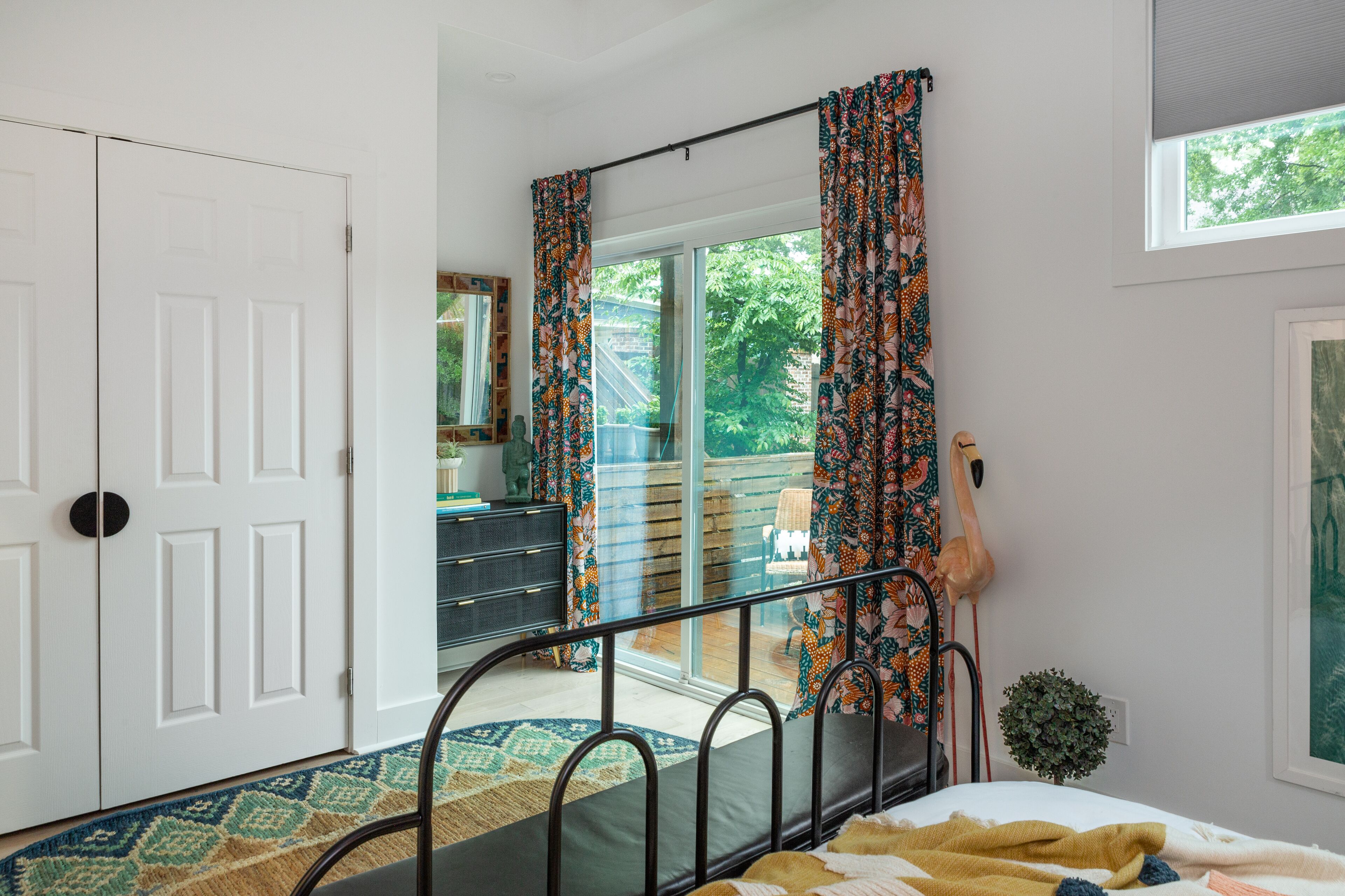 A bedroom with a bed, a dresser, a mirror, and a window with curtains.
