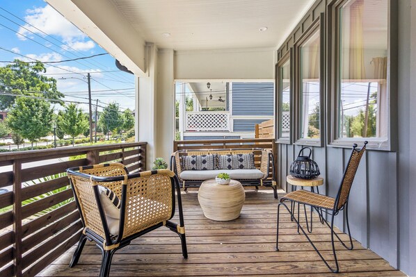 A covered porch with wicker furniture, a round table, and a view of the backyard.