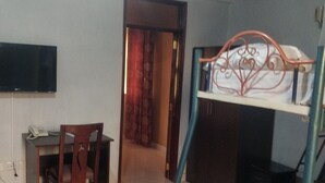A room with a bunk bed, a desk with a chair, a flat-screen TV, and a door leading to another room.