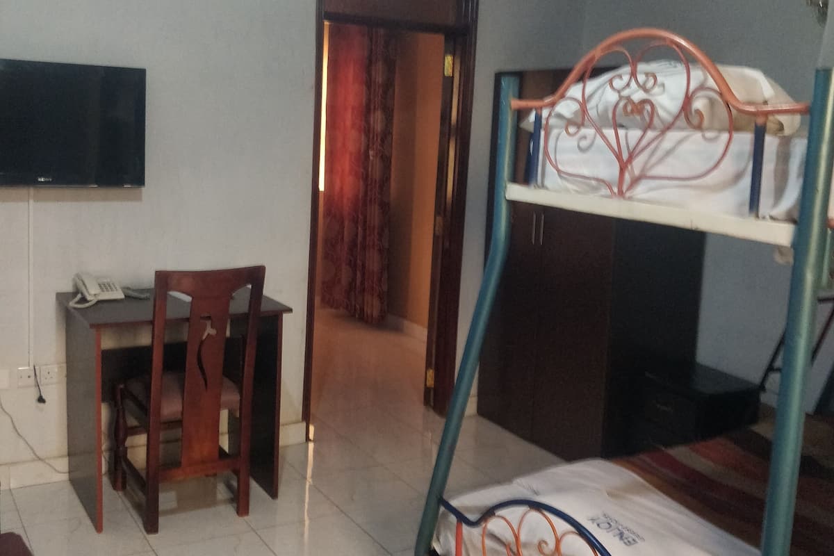 A room with a bunk bed, a desk with a chair, a flat-screen TV, and a door leading to another room.
