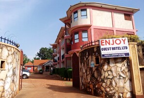 A guest hotel with a reception area, a stone wall entrance, and a sign advertising the hotel. - Enjoy Guest Hotel (Jinja)