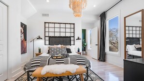 A modern bedroom with a large bed, a decorative headboard, a chandelier, and a large mirror. - Fully Furnished | Fast Wi-Fi | Midterm Stays Welcome (Atlanta)