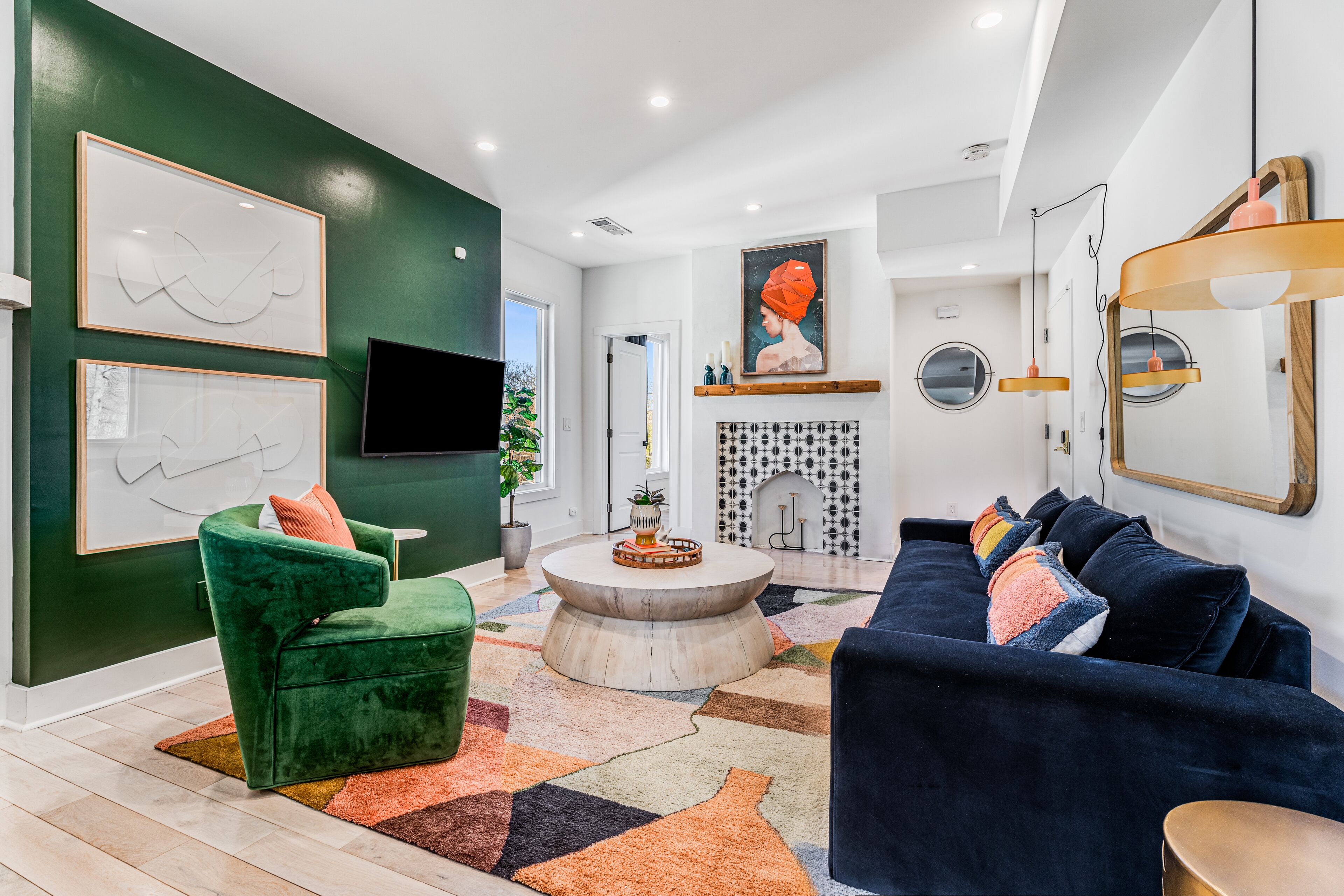 Un salon moderne avec un mur d’accent vert, une table basse ronde, un canapé bleu foncé et un téléviseur à écran plat fixé au mur.