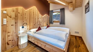 A wooden bedroom with a bed, bedside table, and a window with curtains.