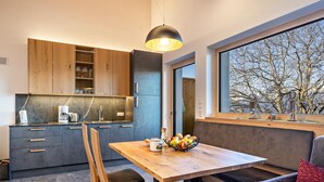 A modern kitchen with wooden cabinets, a marble countertop, and a dining area with a wooden table and bench.