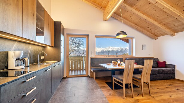 A modern kitchen with wooden cabinets, a built-in coffee maker, and a view of snowy mountains through a window.