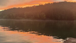 A wooden dock extending over a calm lake with a forested hill in the background. - Come stay on the water and create your own tales to share for a lifetime! (New Tazewell)