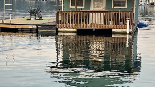A houseboat with a wooden deck and a small balcony, floating on calm water. - Come stay on the water and create your own tales to share for a lifetime! (New Tazewell)