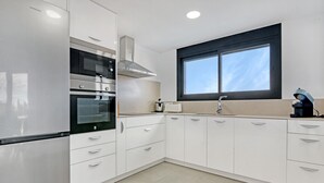 Eine moderne Küche mit Edelstahlgeräten, weißen Schränken und einem Fenster mit schwarzem Rahmen.