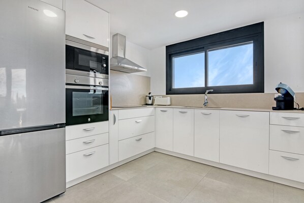 A modern kitchen with stainless steel appliances, white cabinetry, and a window with a black frame.