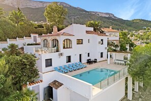 A modern villa with a swimming pool, outdoor seating, and a mountain backdrop.