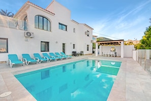 Una piscina amb gandules, una pèrgola i un edifici blanc amb finestres d'arc.