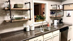 A kitchen with a granite countertop, white cabinets, a dishwasher, and a sink. There are shelves above the countertop holding dishes and glasses. - MAY'S FLOWERS , Stylish 4 Bedroom house, High Speed Internet,  Equipped Kitchen (Tyler)