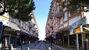 Vista de una calle con edificios de varios pisos, tiendas y cielo despejado.