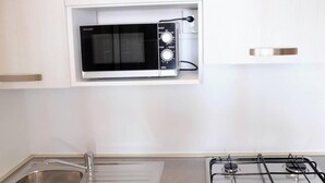 Una cocina con microondas integrado, estufa a gas y pileta de acero inoxidable.