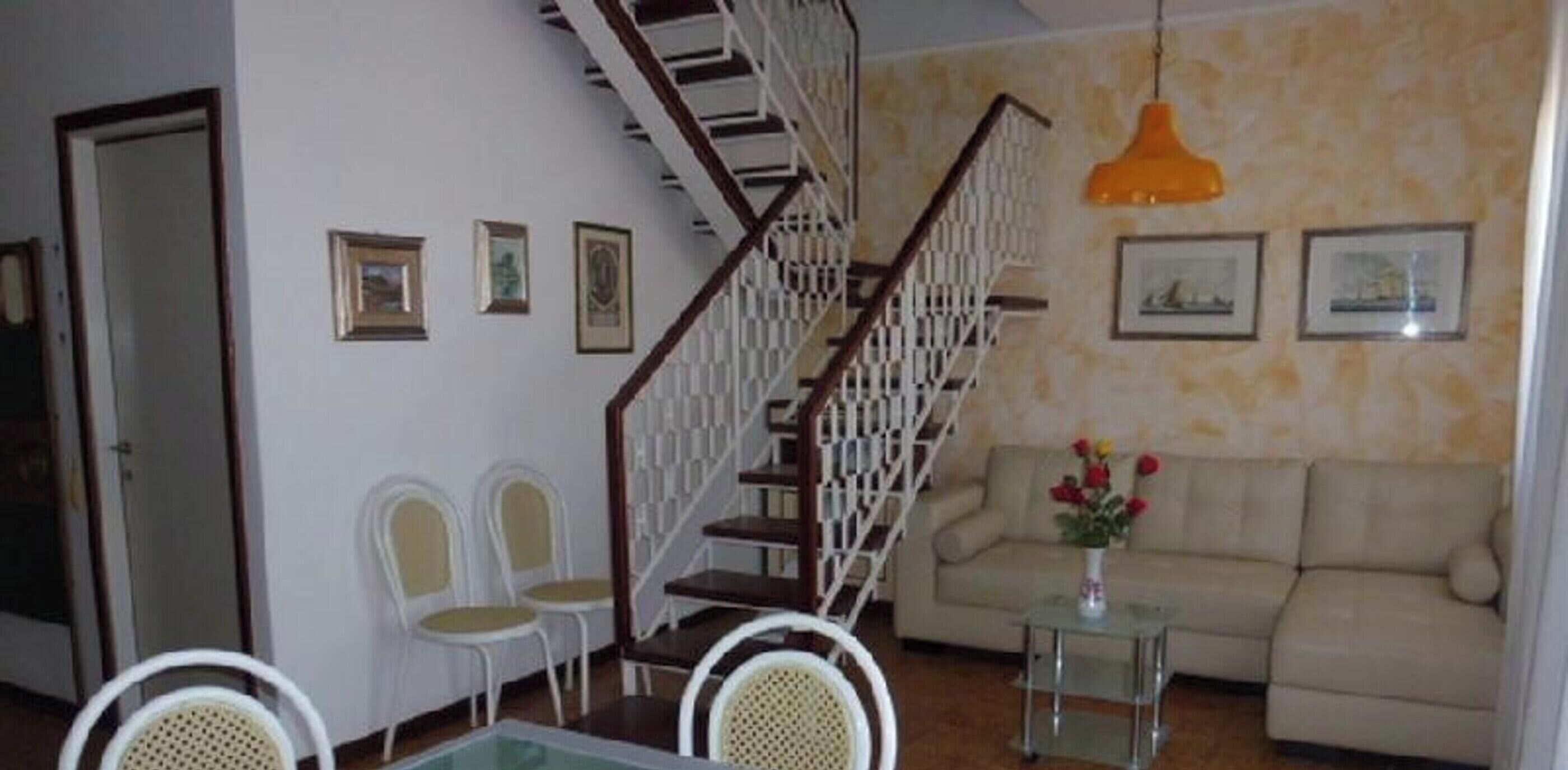 Een woonkamer met een trap, een bank, een salontafel en ingekaderde foto's aan de muur.