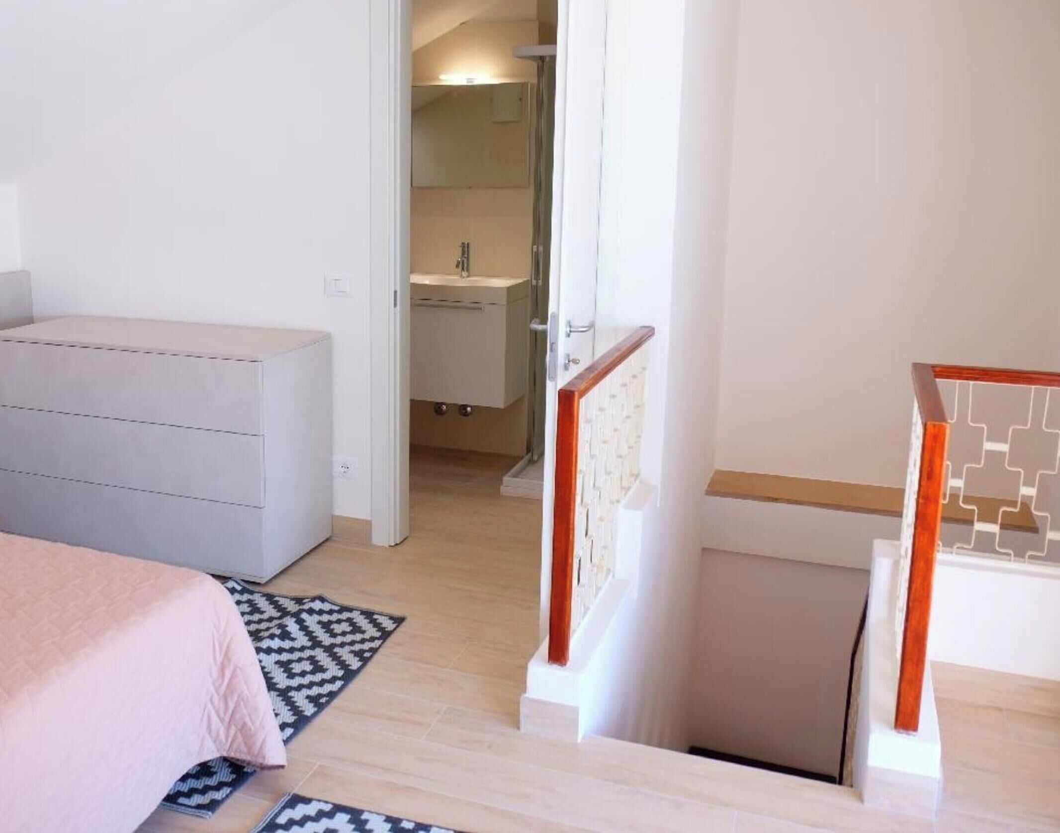 A bedroom with a bed, a dresser, a patterned rug, and a bathroom visible through an open door.