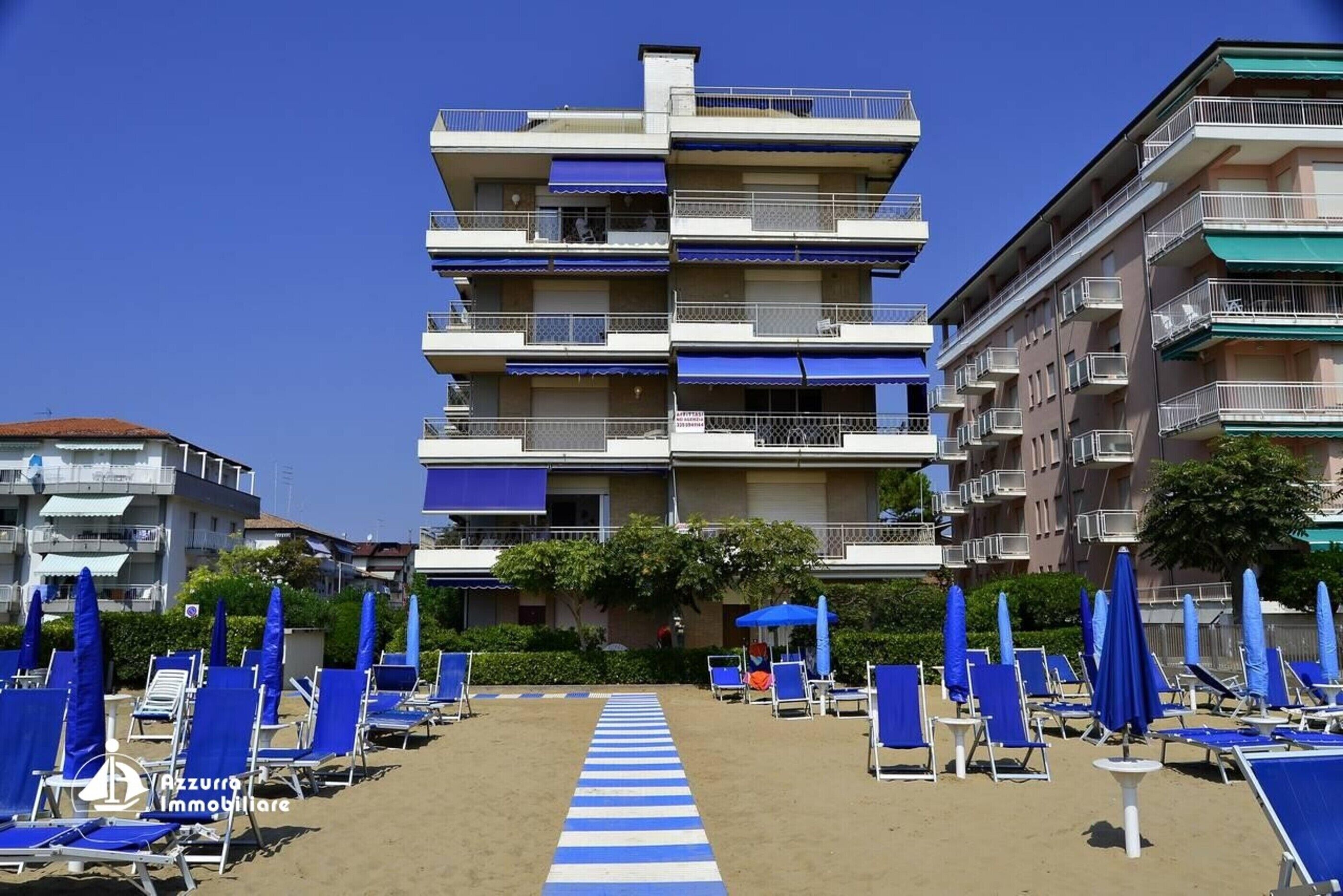 Et hotel ved stranden med flere balkoner, blå strandstole og parasoller.