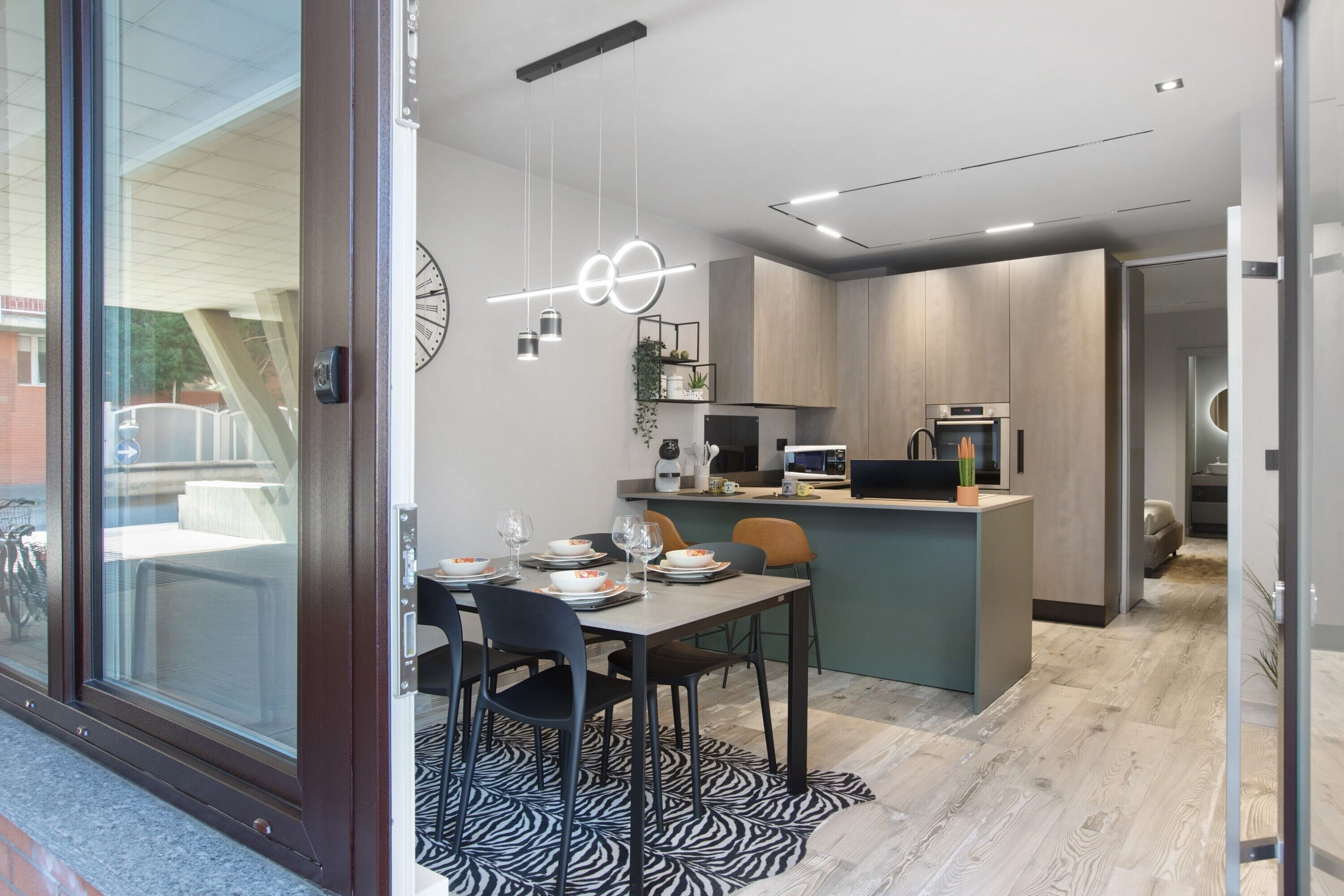 A modern kitchen with a dining area, a built-in island, and a view through a glass door.