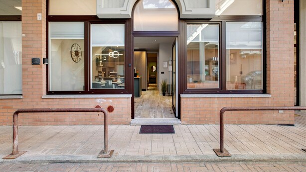 Een gevel van baksteen, grote glasramen en een metalen hekwerk bij de ingang van een gebouw.