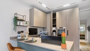Een moderne keuken met een centraal eiland, barkrukken, een koffieapparaat en een plant.