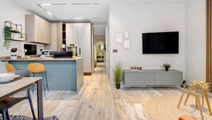 Een moderne keuken met een centraal eiland, een eetgedeelte met stoelen, een aan de muur bevestigde televisie en een kleine potplant.