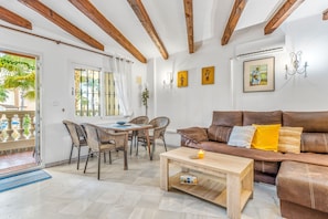 Un salon avec un canapé en cuir marron, une table basse en bois, des chaises en osier et une table à manger.
