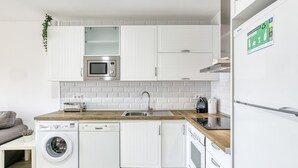 Moderni keittiö, jossa on valkoiset kaapit, sisäänrakennettu mikroaaltouuni, astianpesukone ja jääkaappi.