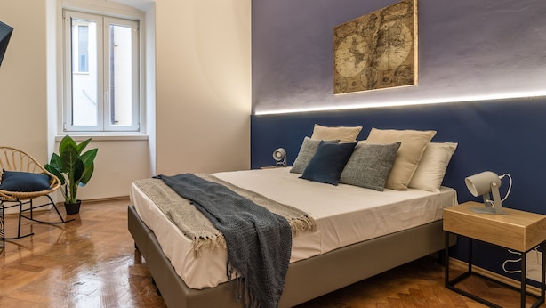 A bedroom with a bed, a desk, a chair, a potted plant, and a window. - Ghiberti Apartments - Prussian Blue (Trieste)