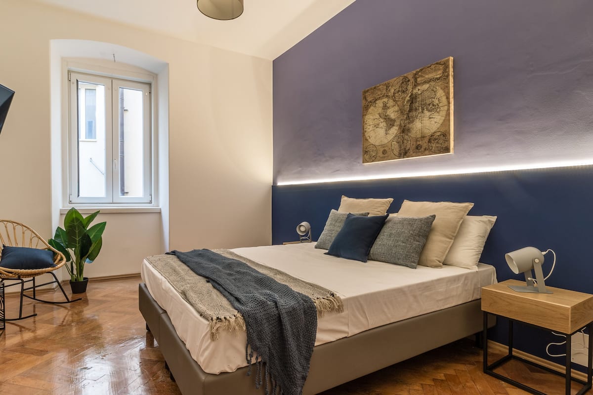 A bedroom with a bed, a desk, a chair, a potted plant, and a window.