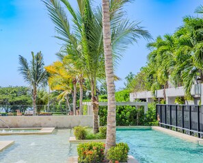 A swimming pool surrounded by palm trees and greenery, with a stone wall and lounge chairs in the background. - Apartmento 2Hab a un paso del Mar (Cartagena)