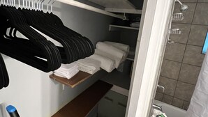 A closet with hanging clothes and shelves, a wooden bench, and a shower area with a curtain. - Coming into town for any special event.Cozy spacious space with all your needs!  (Mount Pleasant)