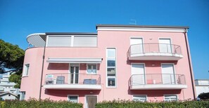 A pink multi-story building with balconies, a door, and a window.