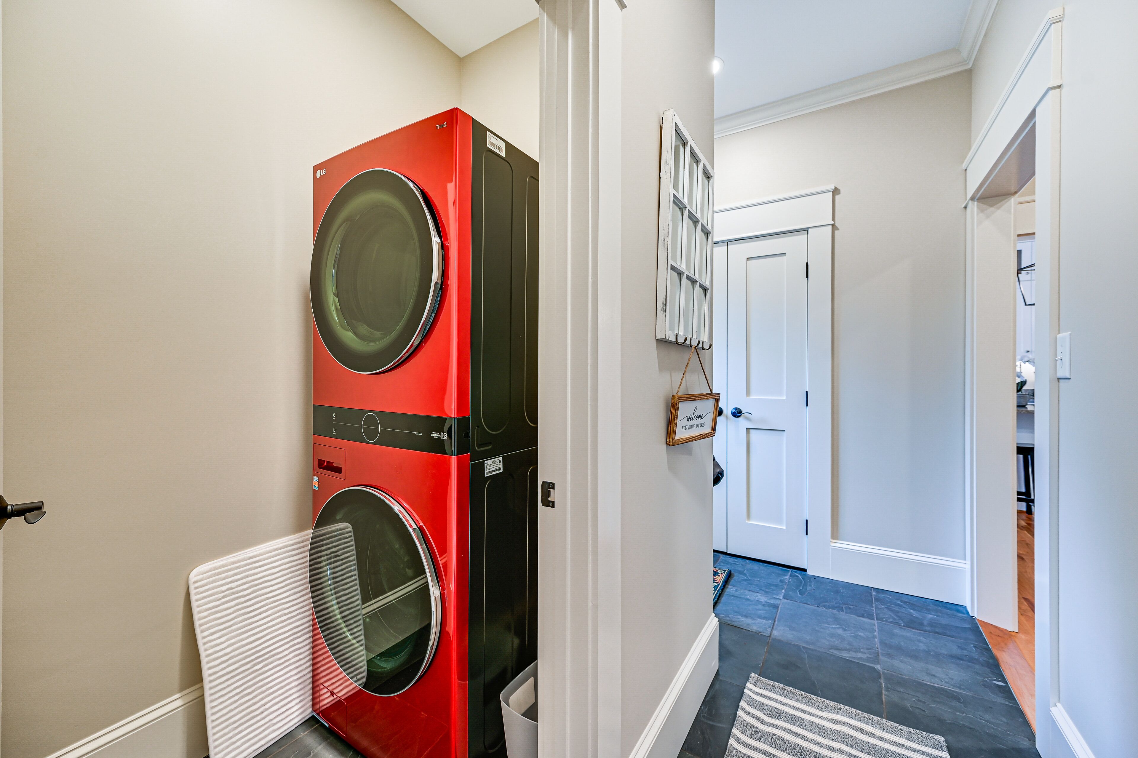 Un área de lavandería con lavadoras y secadoras apiladas, una puerta blanca y un pasillo que conduce a otras habitaciones.