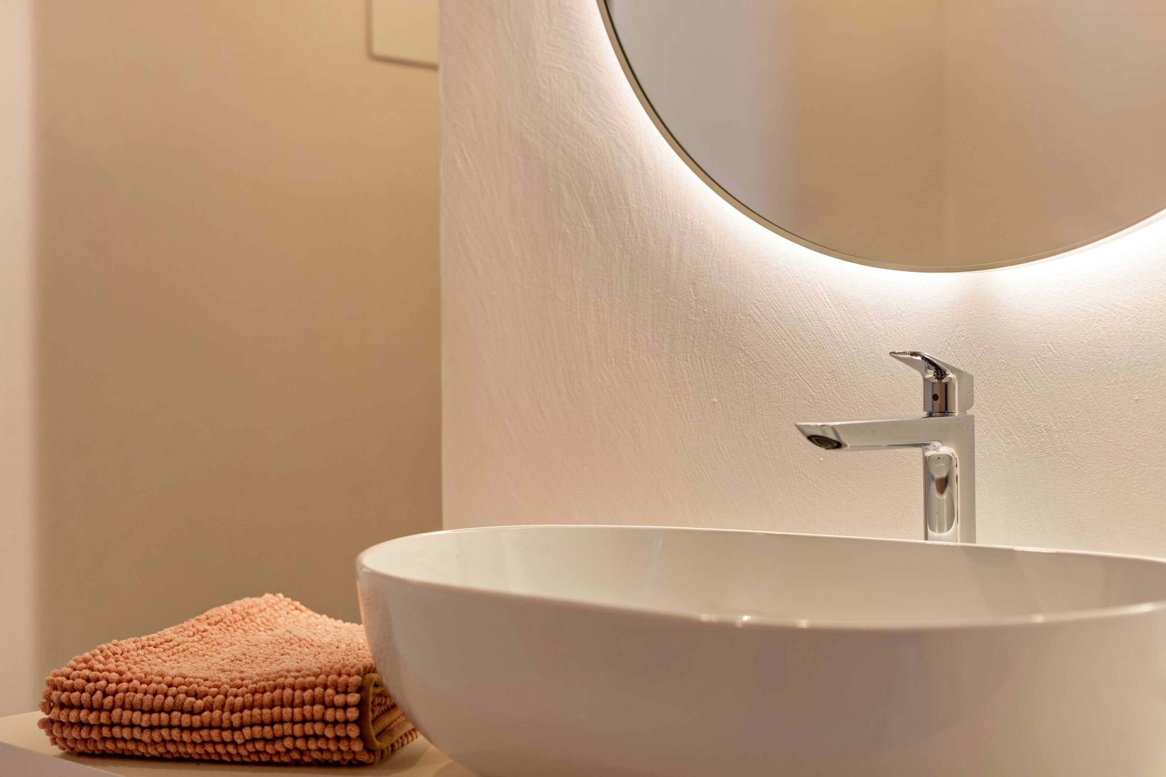 Un bagno con un lavandino bianco, uno specchio tondo e un asciugamano.