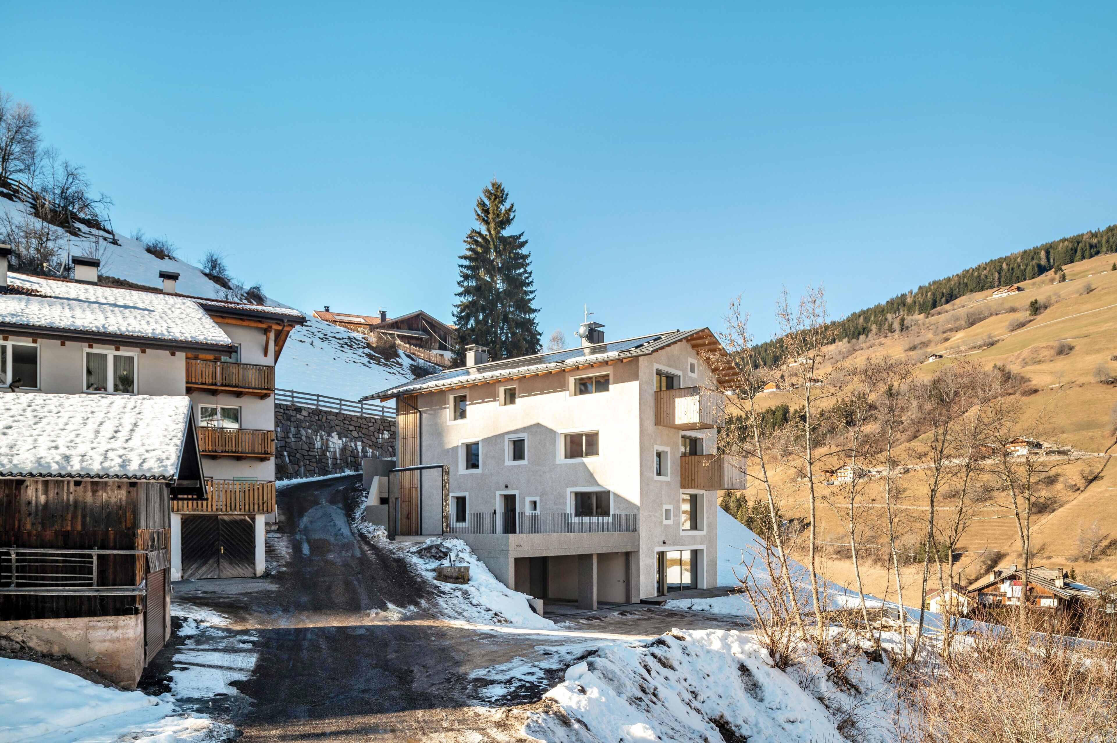 Ein modernes Gebäude mit mehreren Balkonen, einer Steinsäule und einer verschneiten Landschaft.