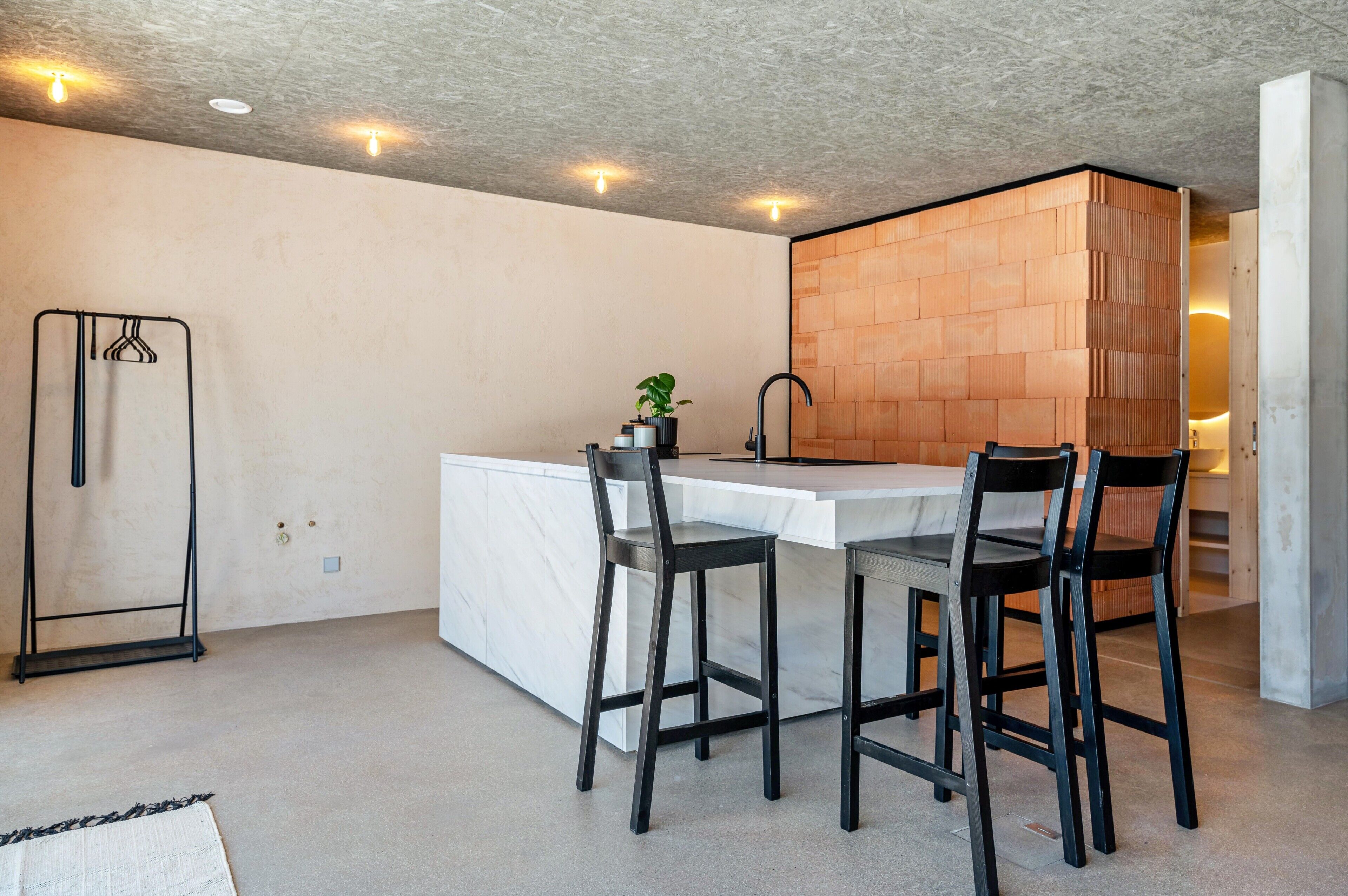 Une cuisine moderne avec un plan de travail en marbre, des tabourets de bar noirs, un étagère suspendue et un mur décoratif en briques.
