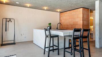 Une cuisine moderne avec un plan de travail en marbre, des tabourets de bar noirs, un étagère suspendue et un mur décoratif en briques.