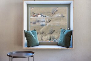 A window seat with two pillows, a small table, and a view of a rural landscape.