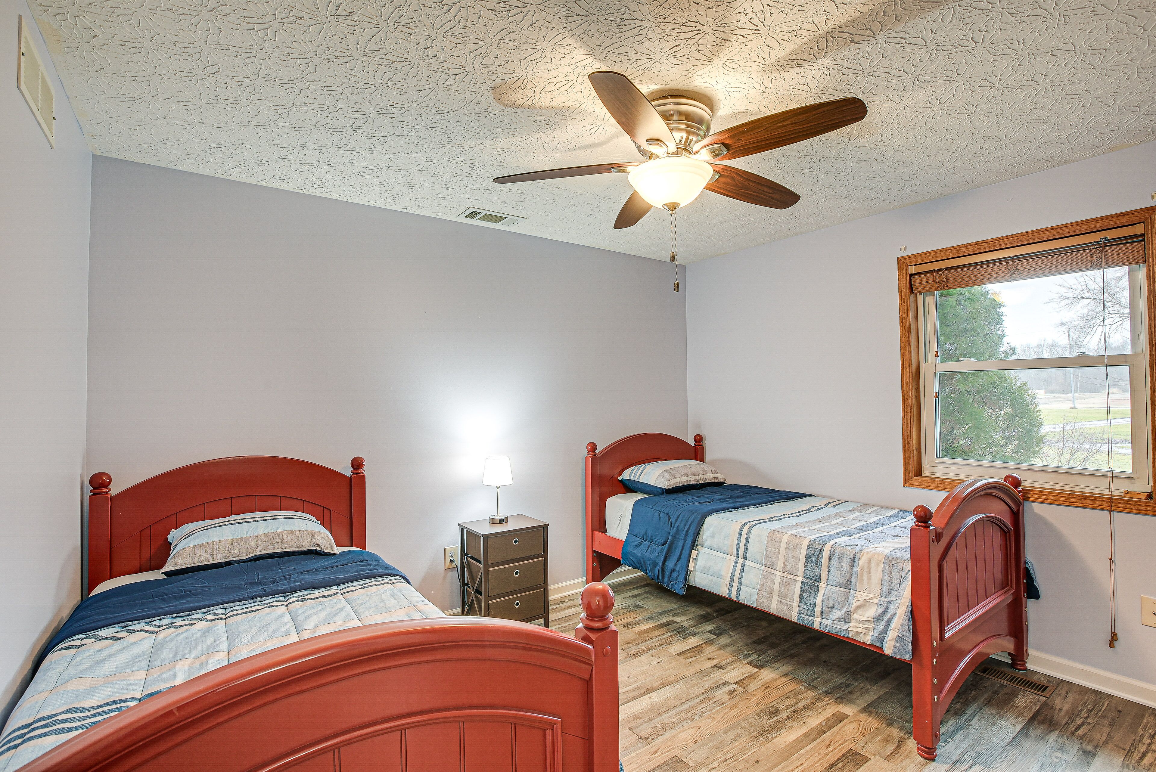 A bedroom with two beds, a ceiling fan, a window, and a nightstand.