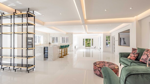 A modern living room with a green sofa, a coffee table, and a glass shelving unit.